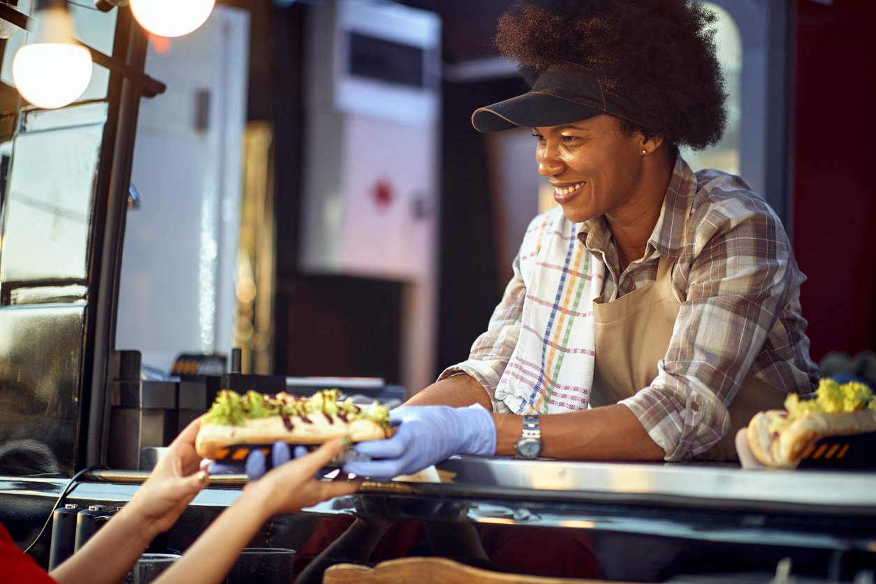 afro-american female employee in fast food service giving sandwiches to a customer with a smile
